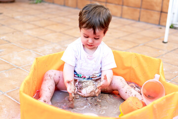 Child playing with sand in an orange plastic pool.