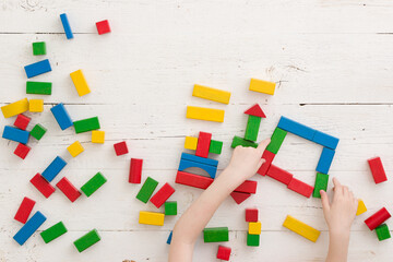 The child builds geometric shapes from wooden multi-colored cubes. Top view on many colored cubes on a white wooden table. Early development and education