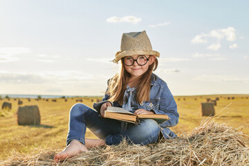 Naklejka na ściany i meble Reading girl sits over the haystack roll on field in countryside. High quality photo. 