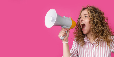 Young woman shouts into a megaphone. Isolated pink background.