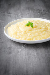 Mashed potatoes in white plate on gray wooden background.