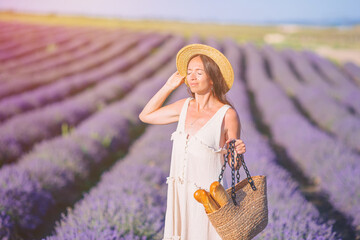 Woman in lavender flowers field at sunset in white dress and hat