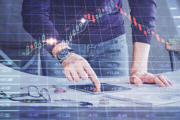 Double exposure of man's hands holding and using a digital device and forex graph drawing. Financial market concept.