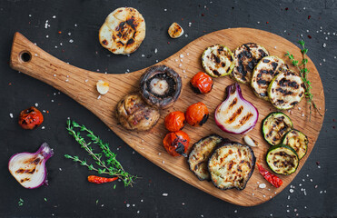 Grilled vegetables on cutting board on  black slate stone background. View from above.
