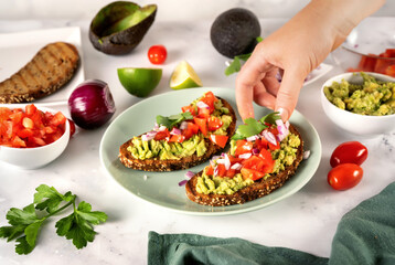 Unrecognisable woman taking a toast from plate with mashed avocado and tomatoe pieces
