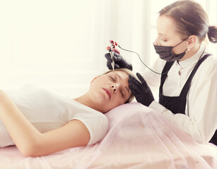 Young woman undergoing procedure of eyebrow permanent makeup in beauty salon