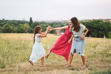Three sister girls playing on the park outdoor. 3 girls, sisters, girlfriends in the field. Happy mother with younger and older daughter, two children plays in the meadow in summer in dresses