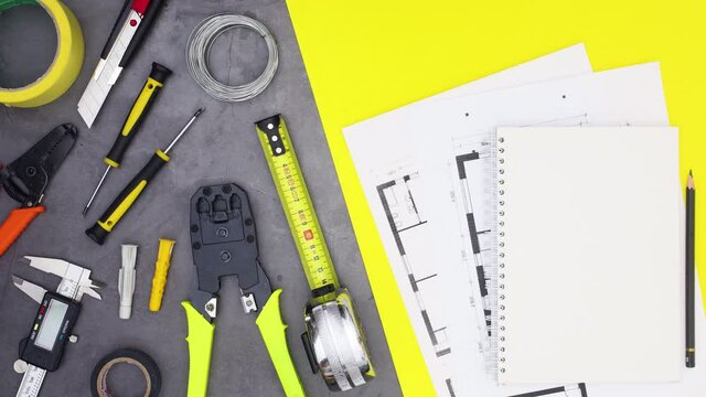 Construction tools and building plans appear on the table. Stop motion 
