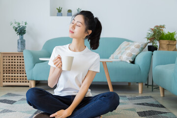 Young asia woman with ponytail in white t-shirt holding a cup of coffee or tea relaxing at home in the morning.