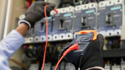 Electrical engineer using digital multi-meter measuring equipment to checking electric current voltage at circuit breaker and cable wiring system in main power distribution board.