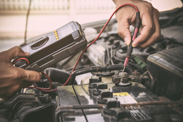 Auto mechanic using measuring equipment tool for fix checking car battery. Concepts of Old car repair service and insurance.