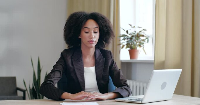 Tired, exhausted Afro girl bored of routine work study in office at home with laptop, loses energy, lays her head on her hands on table, falls asleep long day at workplace, feels sluggishly unhealthy