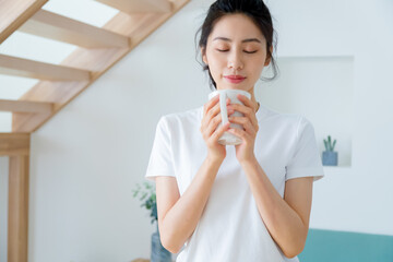 Young asia woman with ponytail in white t-shirt holding a cup of coffee or tea relaxing at home in the morning.