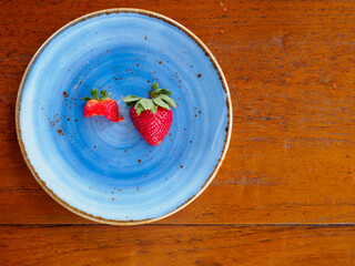 Wide closeup detail of a half-eaten and full strawberry slice on a blue plate and wooden table at a cafe. Bang Sare district, Chonburi, Thailand. Travel and dessert cuisine. - 370282447