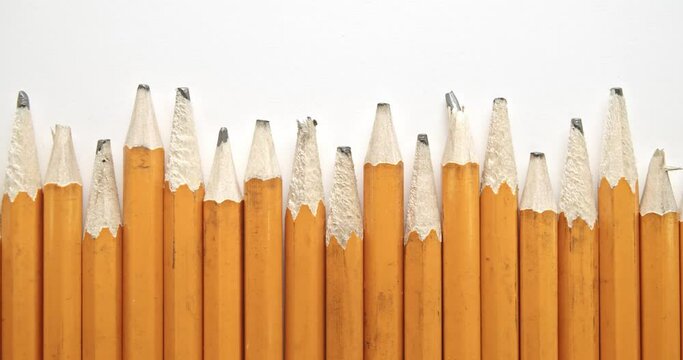 Panning across row of used and worn out yellow pencils with broken pencil tips.