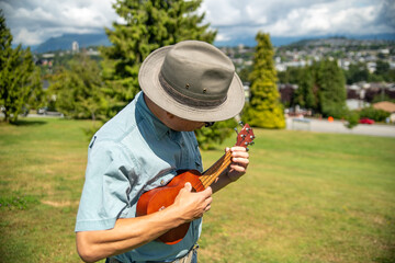 公園で立ってフレットを見ながらウクレレを弾くアジア人男性　　　バンクーバー　ブリティッシュコロンビア　カナダ  © haseg77