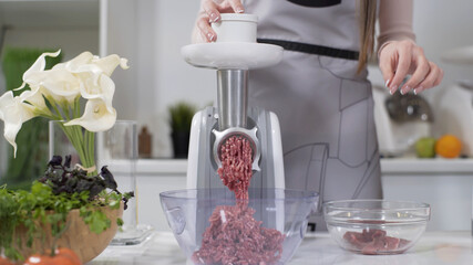 Making minced meat in an electric meat grinder from fresh beef at home. Pile of chopped meat. Electric mincer machine with fresh chopped meat. Preparation of minced beef with an electric meat grinder.