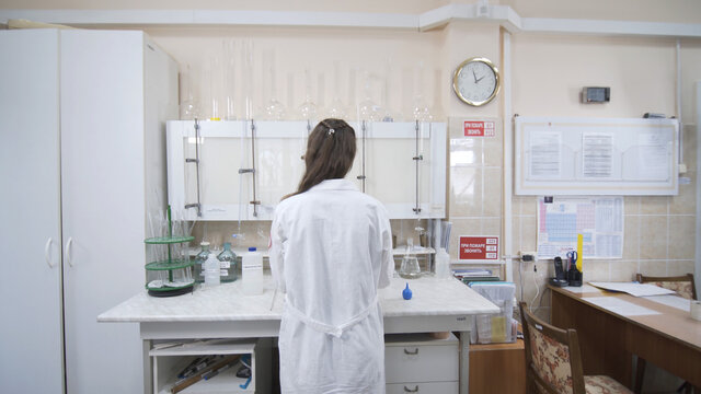 Female scientist analyzes liquid in distillery laboratory researcher. Woman stands with her back to camera. Mixing chemicals and alcoholic beverage.