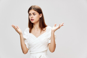 Emotional woman with surprised eyes look to the side holds hands in front of her white dress 