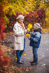 Fototapeta premium Warmly dressed mother and son in the Park after rain in autumn with yellow leaves in their hands