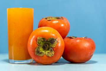 Persimmon juice and fresh fruits on blue background