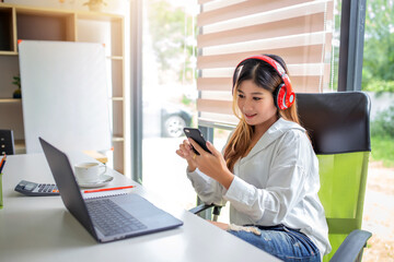 Happy woman. Beautiful young asian woman listening to music with headphones and using laptop computer in a cafe. Concept of listening to music drinking coffee with headphone.