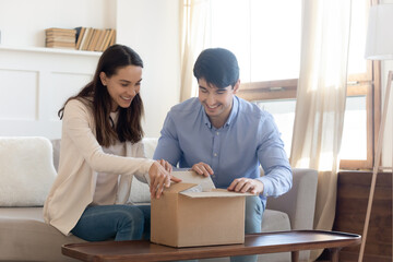 Happy young couple unpacking cardboard box with ordered item from popular internet store, smiling clients satisfied with fast international delivery shipment courier service, online shopping concept - obrazy, fototapety, plakaty