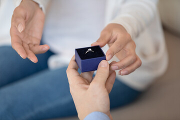 Close up young man holding little box with wedding diamond ring in hands, making proposal to beloved woman. Happy millennial couple planning getting married, engagement marry me romantic moment.