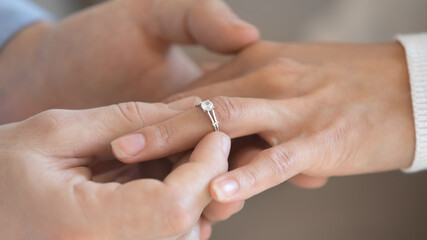 Close up loving young man putting engagement golden ring with diamond on bride finger, wedding proposal acceptance. Affectionate millennial couple in love decided getting married, marry me concept.