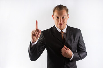 A male businessman in a black suit and tie holds a finger up, points up, on a white background