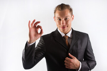 A male businessman in a black suit and tie shows the OK sign with his fingers on a white background