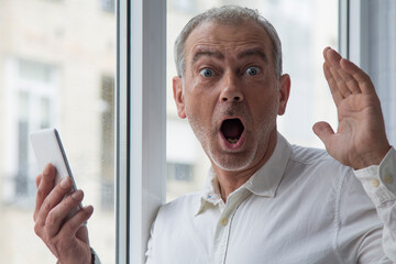 senior man with surprised expression using mobile phone