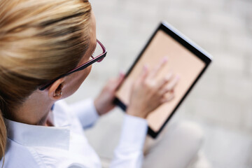 Top view of blonde fashionable businesswoman sitting outdoors and using tablet.