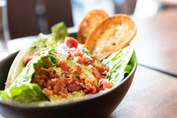 Caesar salad in black bowl on wooden table.