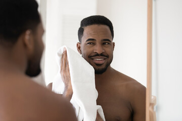 Mirror reflection head shot close up smiling African American man wiping face with white towel...