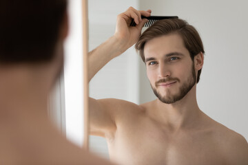 Close up head shot mirror reflection young man combing brushing hair, hairdo and haircut, standing...