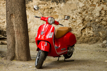 Classic red scooter besides wall.