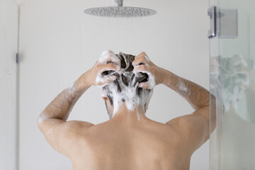 Rear view young man cleaning hair with foamy anti dandruff shampoo close up, standing in modern...