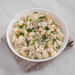 Homemade Macaroni Salad in a white bowl on a white wooden background, low angle view. Close-up.