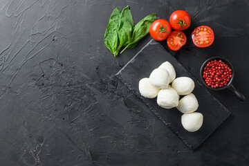 Fototapeta na wymiar Fresh cherry tomatoes, basil leaf, mozzarella cheese on black slate stone chalkboard Healthy Italian traditional caprese salad ingredients. 