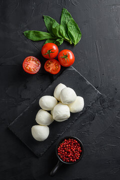 Fresh cherry tomatoes, basil leaf, mozzarella cheese on black slate stone chalkboard  Organic Mediterranean food concept, flat lay space for text vertical