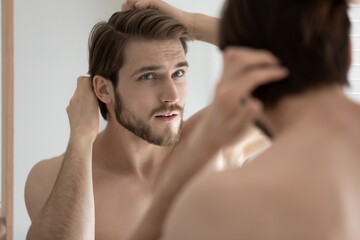 Close up head shot anxious stressed young man touching head, checking hair, looking in mirror,...
