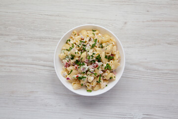 Homemade Macaroni Salad in a white bowl on a white wooden table, top view. Flat lay, overhead, from above.