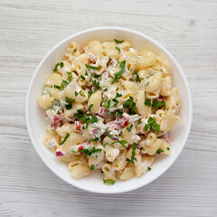 Homemade Macaroni Salad in a white bowl on a white wooden surface, top view. Flat lay, overhead, from above.