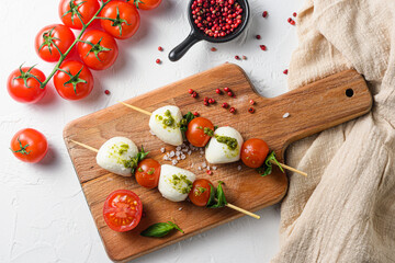 Caprese salad on sticks Cherry tomatoes, mozzarella cheese, basil, pesto sauce on wood board over white rustic background top view