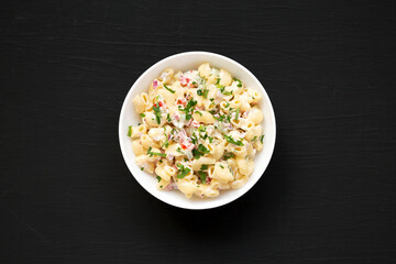 Homemade Macaroni Salad in a white bowl on a black background, top view. Flat lay, overhead, from above.