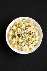 Homemade Macaroni Salad in a white bowl on a black background, top view. Flat lay, overhead, from above.