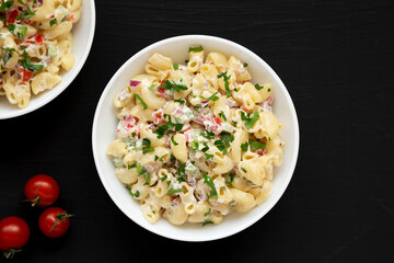 Homemade Macaroni Salad in a white bowl on a black background, top view. Flat lay, overhead, from above. Copy space.