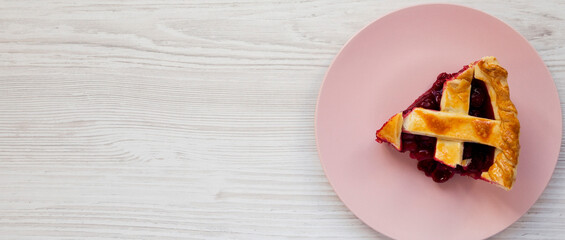 Slice of Yummy Homemade Cherry Pie on a pink plate on a white wooden surface, top view. Flat lay, overhead, from above. Copy space.