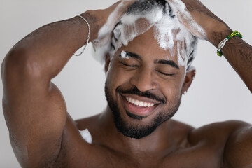 Close up smiling African American handsome young man washing cleaning hair with foamy anti-dandruff...
